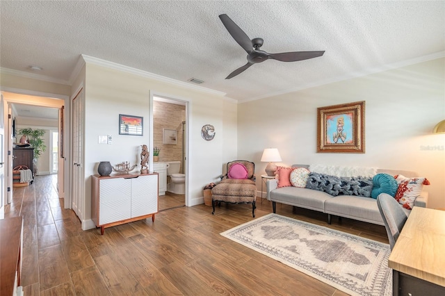 living area with a textured ceiling, visible vents, wood finished floors, and ornamental molding