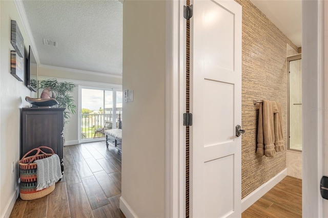 hall featuring crown molding, visible vents, a textured ceiling, wood finished floors, and baseboards