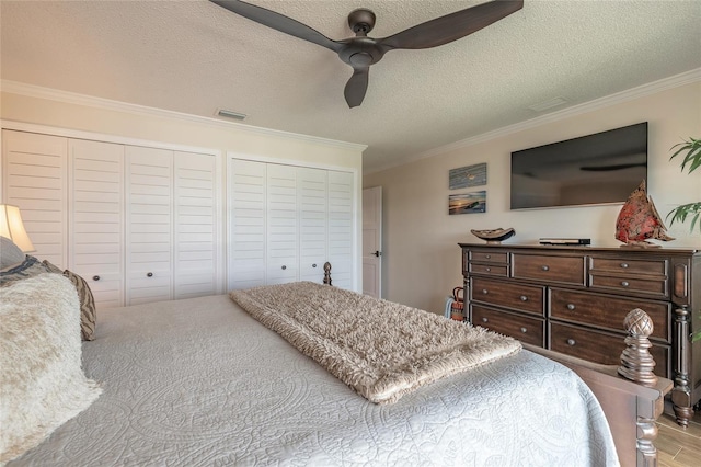 bedroom with multiple closets, visible vents, ornamental molding, a ceiling fan, and a textured ceiling