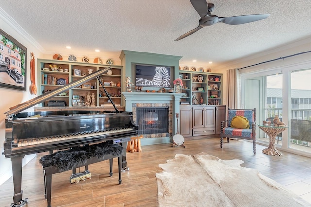 sitting room featuring a tiled fireplace, wood finished floors, a ceiling fan, and crown molding