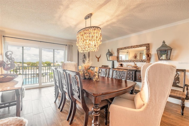 dining space with ornamental molding, a textured ceiling, light wood finished floors, and an inviting chandelier