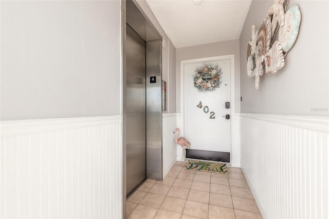 entryway with a wainscoted wall, a textured ceiling, elevator, and light tile patterned flooring