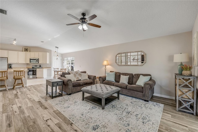 living room with a textured ceiling, light wood-style flooring, a ceiling fan, baseboards, and vaulted ceiling