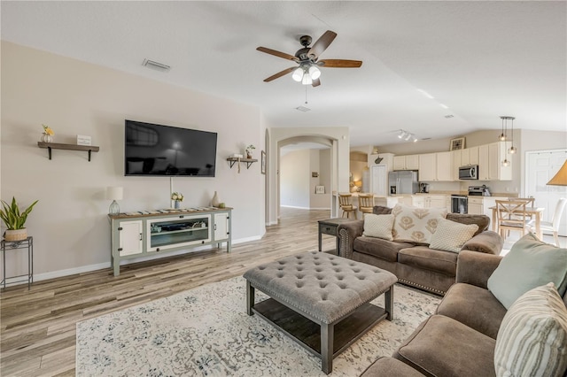 living area featuring arched walkways, ceiling fan, lofted ceiling, light wood-style flooring, and visible vents