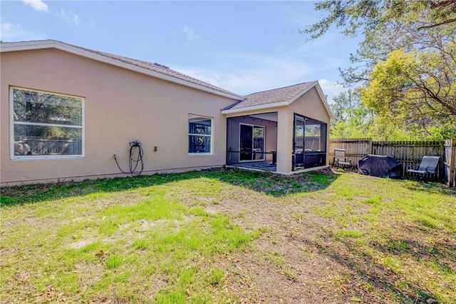 back of house with a sunroom, fence, a lawn, and stucco siding