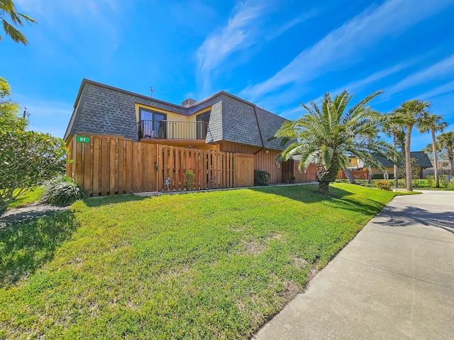 view of front of property with roof with shingles, mansard roof, a front lawn, and fence