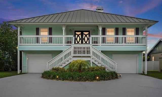 raised beach house with covered porch, an attached garage, and a standing seam roof