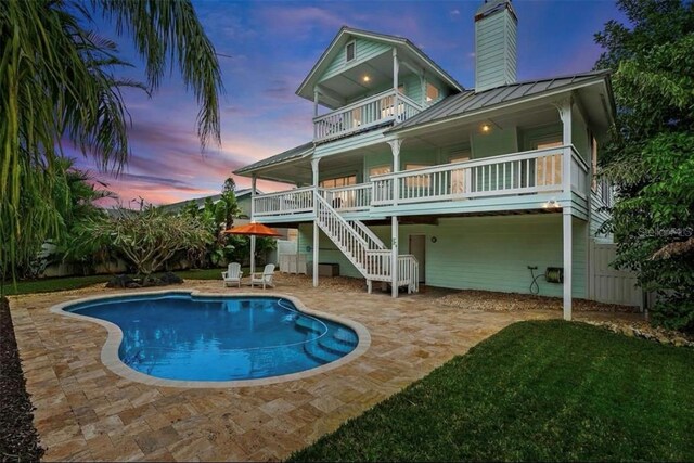 back of property at dusk featuring a standing seam roof, metal roof, a balcony, a chimney, and a patio area