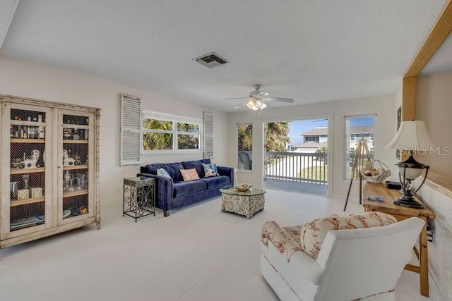 living area with a ceiling fan, visible vents, plenty of natural light, and a textured ceiling