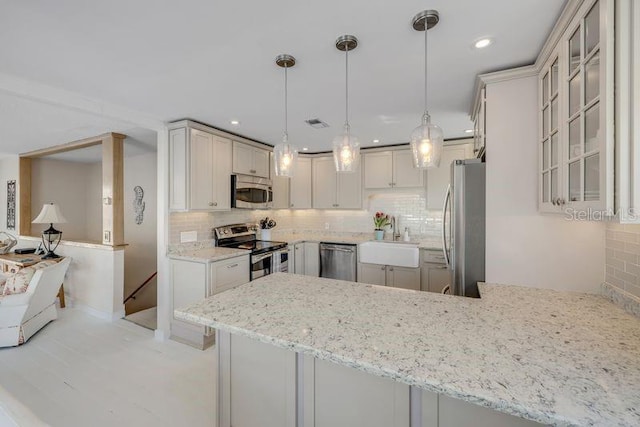 kitchen with tasteful backsplash, light stone counters, a peninsula, stainless steel appliances, and a sink