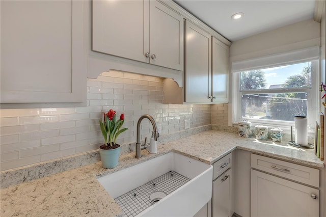 kitchen featuring tasteful backsplash, light stone counters, a sink, and recessed lighting