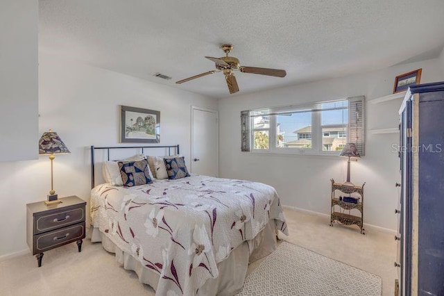 bedroom with a textured ceiling, light colored carpet, a ceiling fan, baseboards, and visible vents