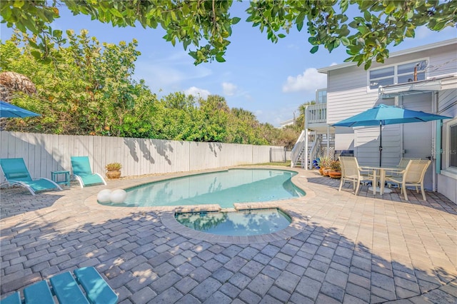 view of pool featuring a patio, a pool with connected hot tub, stairway, outdoor dining space, and a fenced backyard