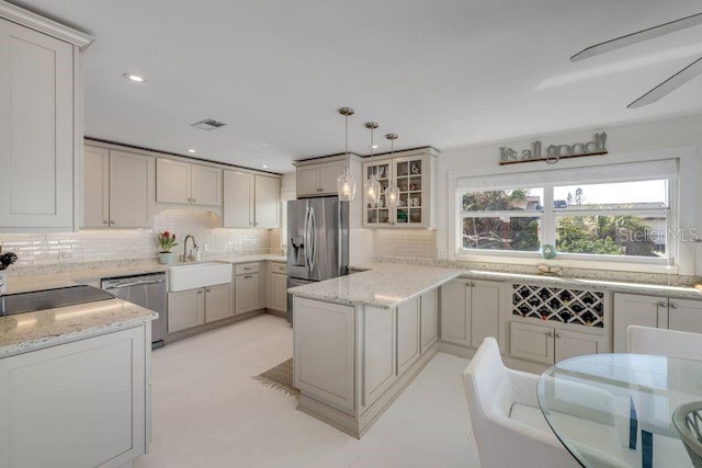 kitchen with appliances with stainless steel finishes, a sink, light stone counters, and tasteful backsplash