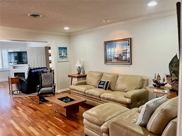 living area featuring ornamental molding, visible vents, a fireplace, and wood finished floors