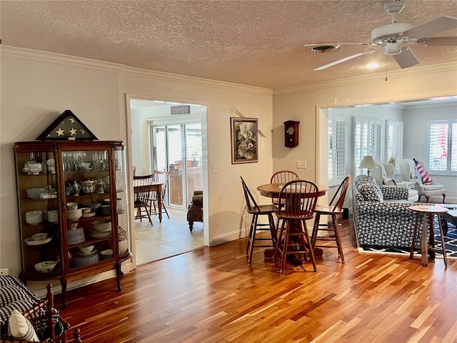 dining room with light wood finished floors, visible vents, a ceiling fan, ornamental molding, and a textured ceiling