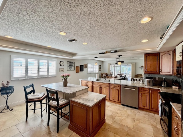 kitchen with appliances with stainless steel finishes, brown cabinets, a peninsula, a tray ceiling, and a sink