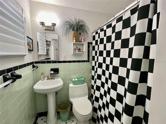 full bathroom featuring a textured ceiling, toilet, wainscoting, and tile walls