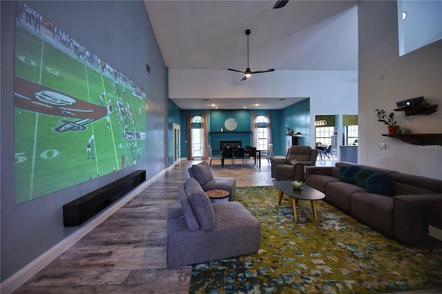 living room with baseboards, a ceiling fan, wood finished floors, a fireplace, and high vaulted ceiling