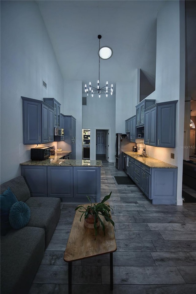 kitchen with high vaulted ceiling, dark wood finished floors, a sink, and a chandelier