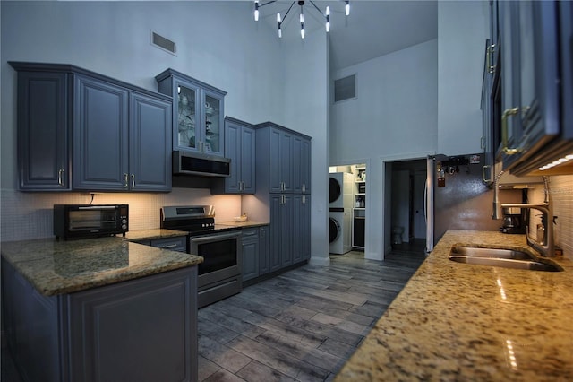 kitchen featuring blue cabinets, stainless steel appliances, a sink, and stacked washer and clothes dryer