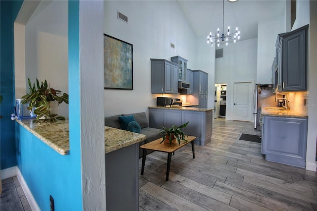 kitchen featuring light wood-style flooring, visible vents, light stone counters, and a notable chandelier