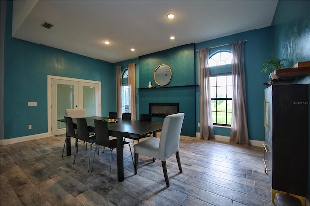 dining space featuring a large fireplace, wood finished floors, visible vents, baseboards, and french doors