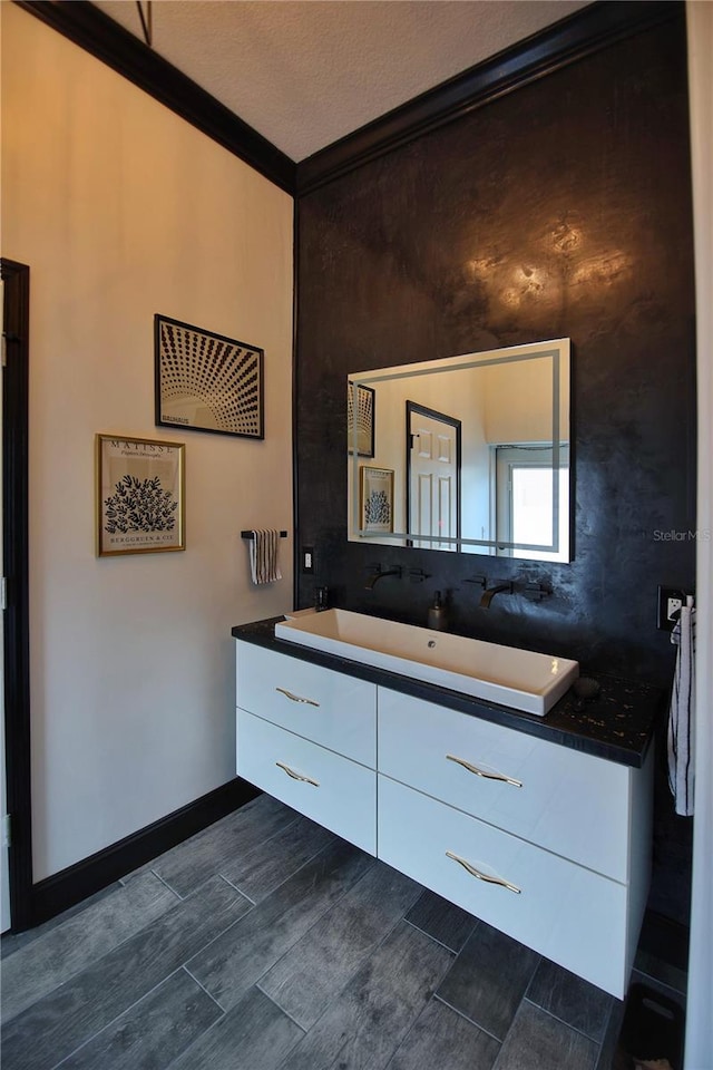 bathroom with baseboards, wood finish floors, vanity, and crown molding