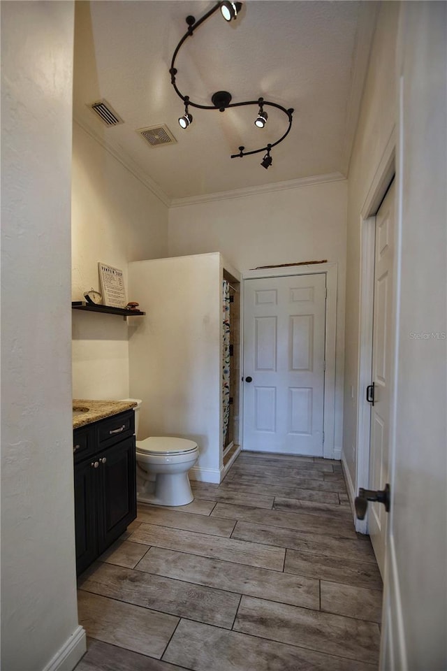 bathroom featuring wood finish floors, vanity, toilet, and crown molding