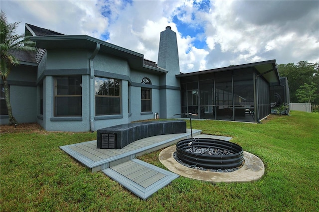 back of house with a fire pit, a sunroom, a lawn, stucco siding, and a chimney