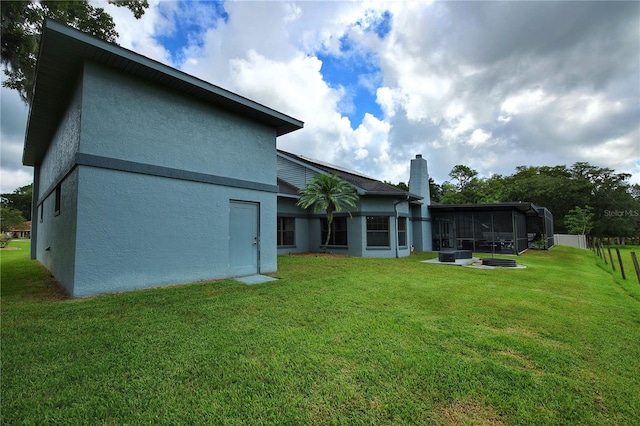 rear view of property featuring a yard, a chimney, a sunroom, and stucco siding