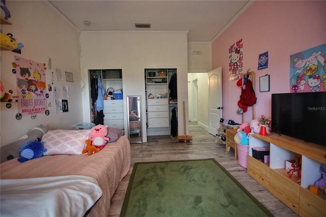 bedroom with ornamental molding, visible vents, multiple closets, and wood finished floors