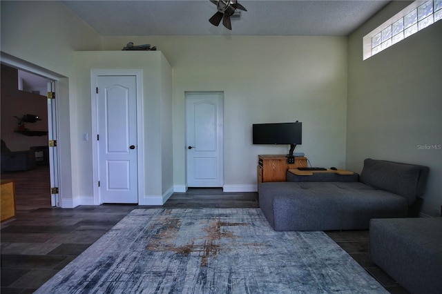 living area featuring a ceiling fan, a textured ceiling, baseboards, and wood finished floors