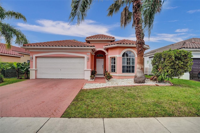 mediterranean / spanish house with an attached garage, a tile roof, decorative driveway, stucco siding, and a front lawn