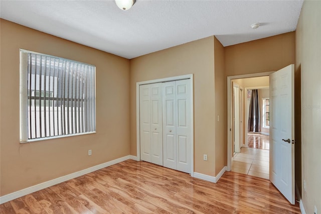 unfurnished bedroom with a closet, multiple windows, light wood-style flooring, and baseboards