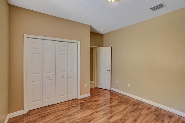 unfurnished bedroom featuring a closet, visible vents, light wood-style flooring, a textured ceiling, and baseboards