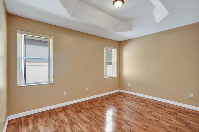 unfurnished room with light wood finished floors, baseboards, and a raised ceiling