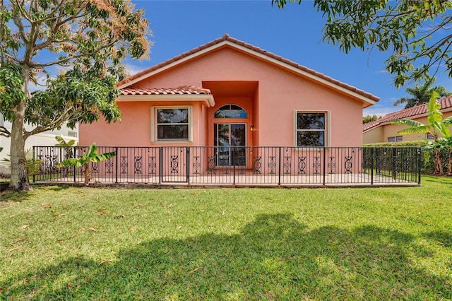 rear view of property featuring a lawn, a tile roof, fence, and stucco siding