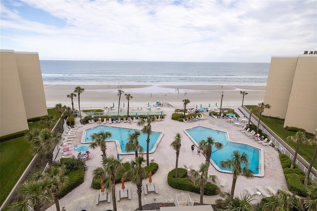 community pool with a patio area, a water view, and a view of the beach