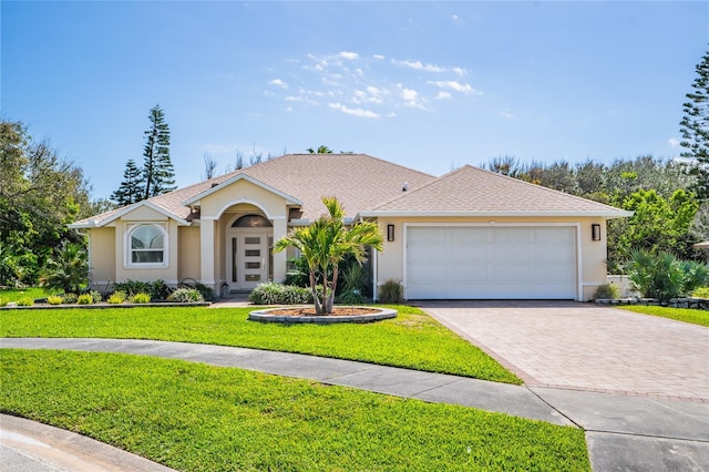 view of front of home with a shingled roof, an attached garage, decorative driveway, a front lawn, and stucco siding