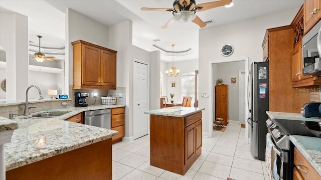 kitchen featuring ceiling fan with notable chandelier, stainless steel appliances, a sink, backsplash, and brown cabinetry