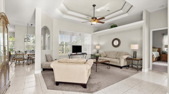 living room with light tile patterned floors, a raised ceiling, a ceiling fan, and a healthy amount of sunlight