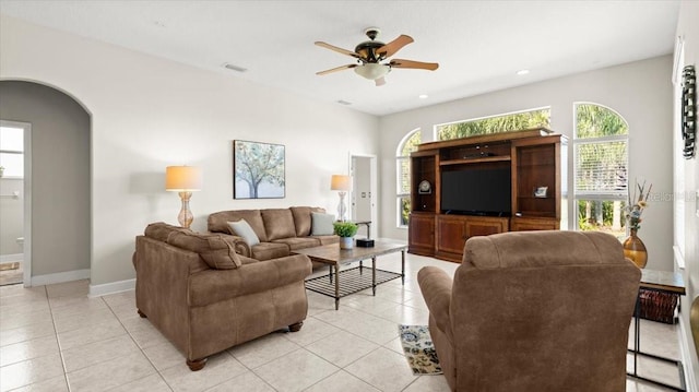 living area with light tile patterned floors, visible vents, arched walkways, baseboards, and ceiling fan