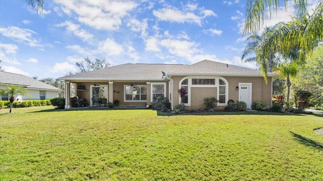 rear view of property featuring ceiling fan, a yard, and stucco siding