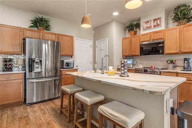 kitchen featuring tasteful backsplash, appliances with stainless steel finishes, light wood-type flooring, a kitchen bar, and a sink