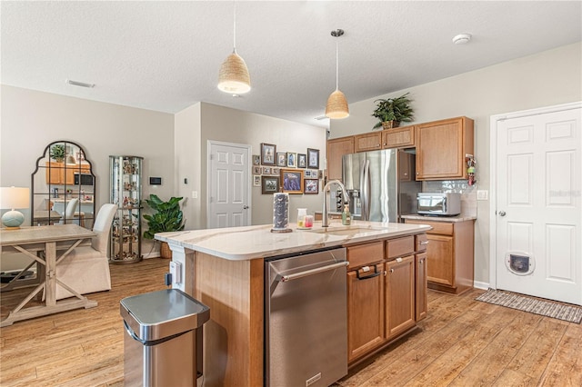 kitchen featuring stainless steel appliances, light countertops, light wood-style floors, a kitchen island with sink, and a sink