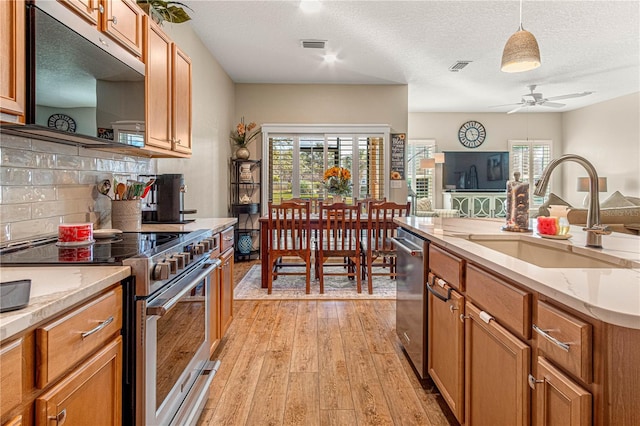 kitchen with a sink, visible vents, appliances with stainless steel finishes, light wood finished floors, and brown cabinetry