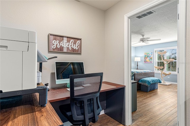 office space with baseboards, visible vents, ceiling fan, wood finished floors, and a textured ceiling