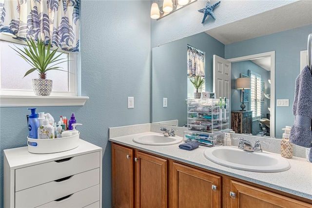 bathroom with double vanity, a textured ceiling, a sink, and a textured wall