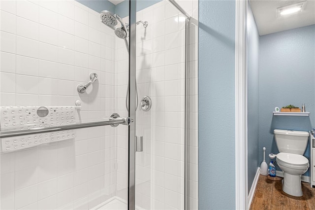 bathroom featuring wood finished floors, a shower stall, toilet, and baseboards